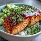 A close-up of a Bang Bang Salmon Bowl showing golden salmon, fresh greens, and a spicy white drizzle.