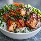 Healthy Baked Salmon Rice Bowl with avocado slices and edamame, drizzled with creamy sriracha mayo and sprinkled with toasted sesame seeds.