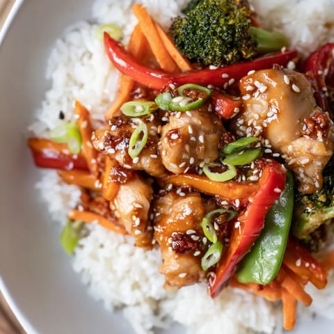A steaming teriyaki chicken bowl, showcasing chicken and bright vegetables, topped with sesame seeds.