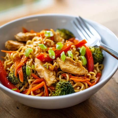 A close-up of Spicy Ramen Stir-Fry featuring glossy noodles tossed with vibrant red bell peppers and fresh broccoli.