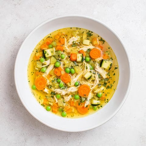 A close-up of steaming Spring Garden Chicken Soup, featuring bright carrots and zucchini in a clear, aromatic herb-infused broth.