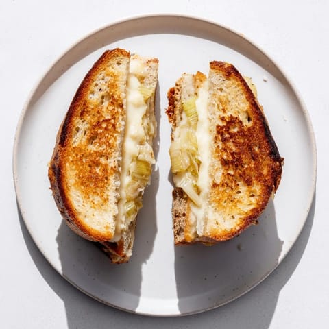 Golden-brown Havarti & Caramelized Leek Grilled Cheese slices ooze melted cheese on a rustic plate.