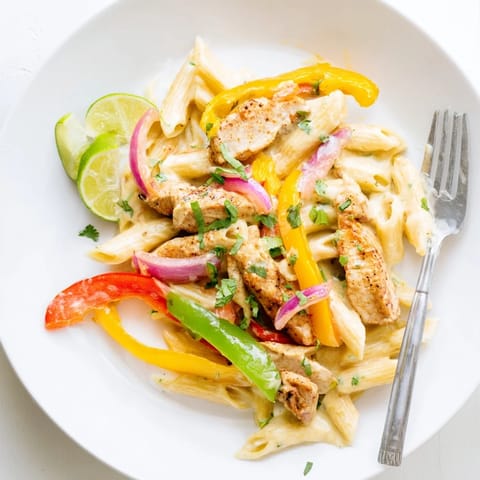 A vibrant skillet of Fajita Chicken Pasta, featuring golden-brown spiced chicken strips nestled among sautéed red, yellow, and green bell peppers in a rich, creamy sauce.