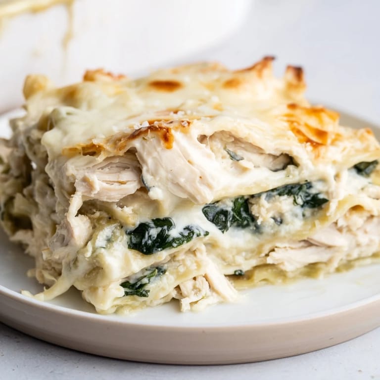 A hearty slice of Chicken Alfredo Lasagna reveals layers of spinach, ricotta, and golden, bubbly cheese topping.