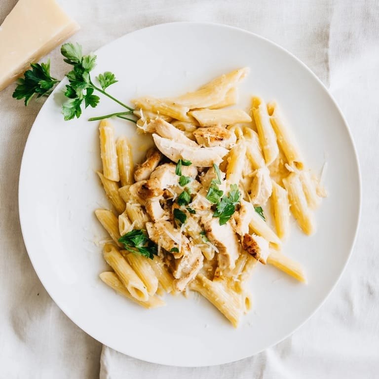 A close-up of Roasted Garlic Chicken Penne highlights the tender chicken and silken, oven-roasted garlic cream sauce clinging to each pasta tube.