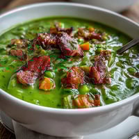 A steaming bowl of creamy Split Pea Soup, garnished with fresh thyme and a crusty bread slice for dipping.
