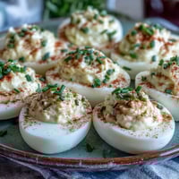 Golden Million Dollar Deviled Eggs garnished with paprika and fresh chives on a serving platter, ready for a party.