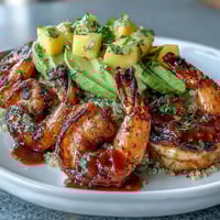 Grilled shrimp with smoky paprika sits next to creamy avocado slices and fluffy quinoa in a bright bowl, all topped with mango salsa and a drizzle of lime chili sauce.